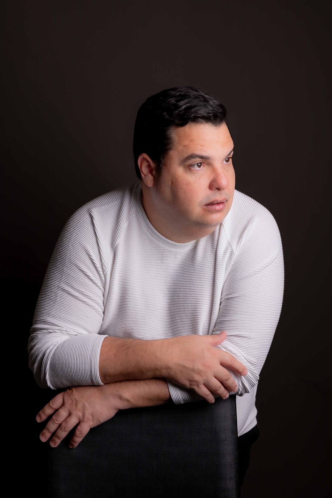 Diogo Garcia de suéter branco, apoiado no encosto de uma cadeira, olhando para o lado